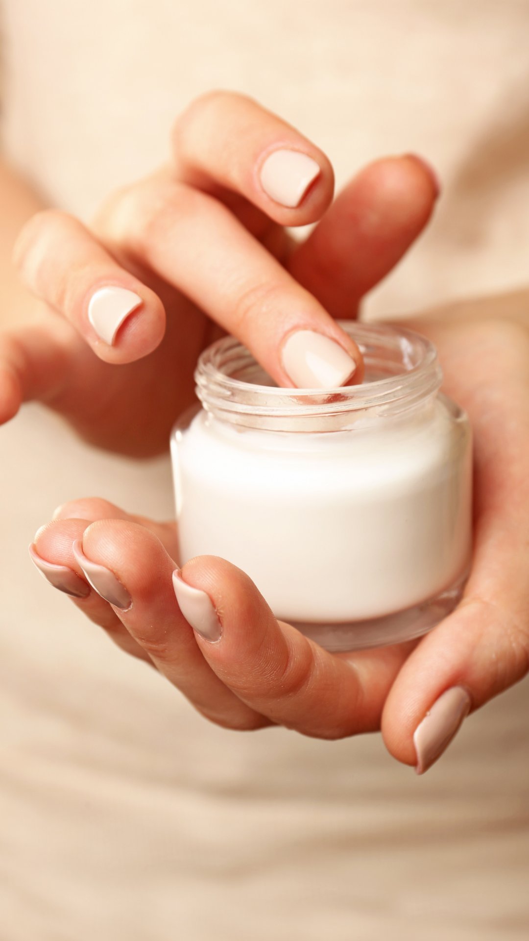 A person holding a jar of cream in their hands.