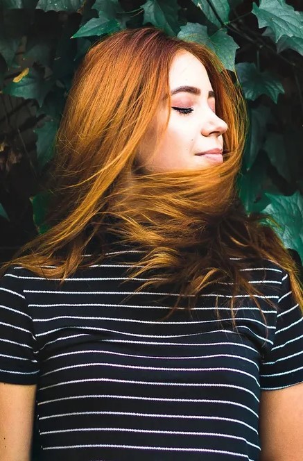 Redhead woman in striped shirt, eyes closed.